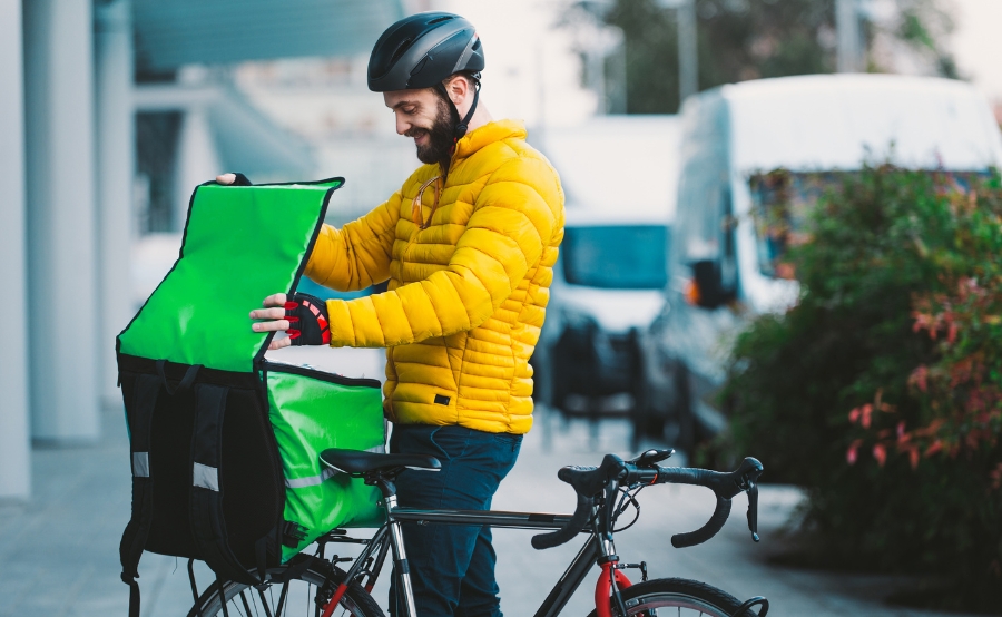 A delivery cyclist in a yellow jacket checks his bag, reflecting how new Boston regulations are drawing reactions from all sides