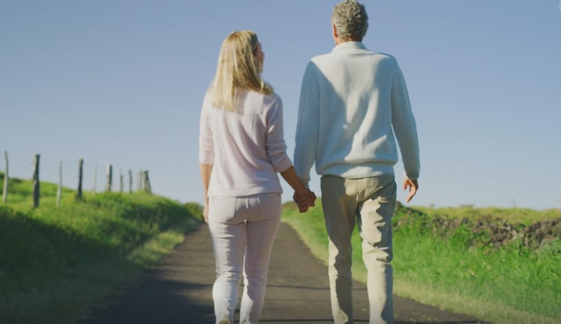 A couple walks hand-in-hand down a country road, bathed in sunlight