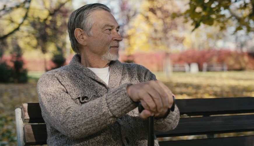 An older man sits thoughtfully on a park bench