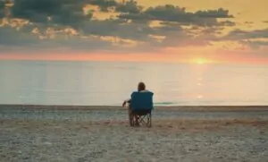 Golden hour paints the sky, while a solitary figure sits on the beach