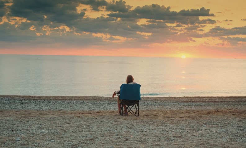 Golden hour paints the sky, while a solitary figure sits on the beach