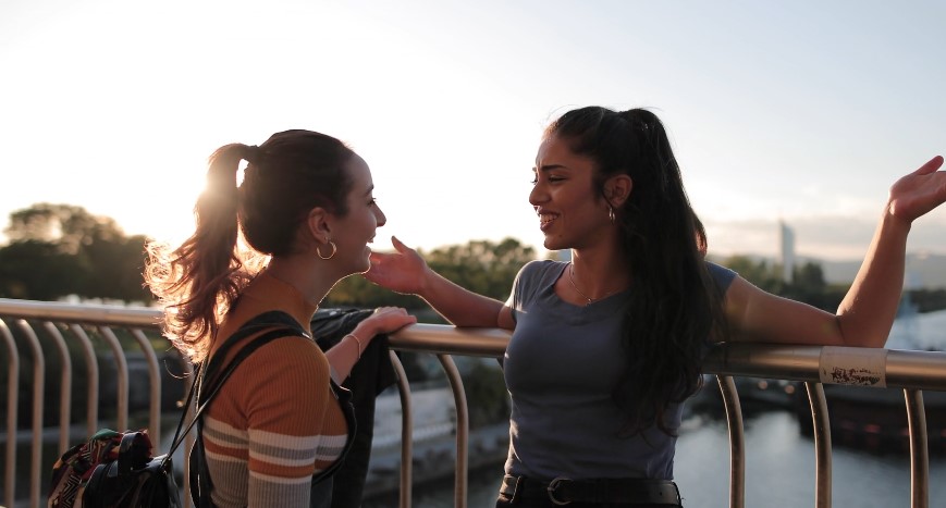 Two young women engage in conversation, bathed in the golden light of sunset