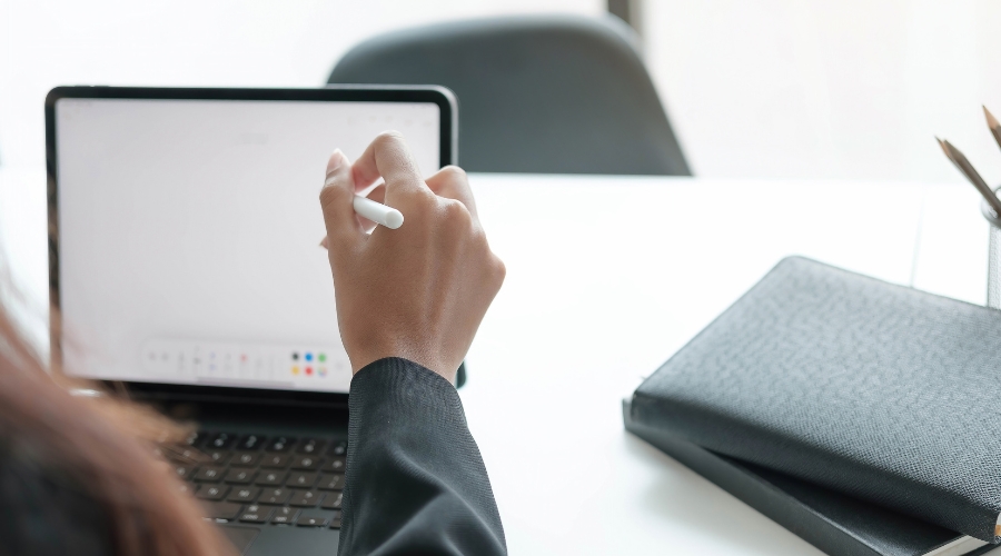 A person uses a stylus on a tablet at a desk, symbolizing digital tools that support human rights campaigns