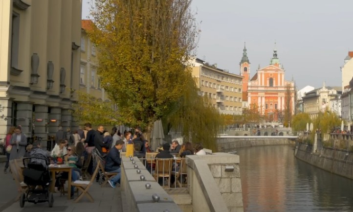 People seated at tables along a picturesque canal in a city in Slovenia