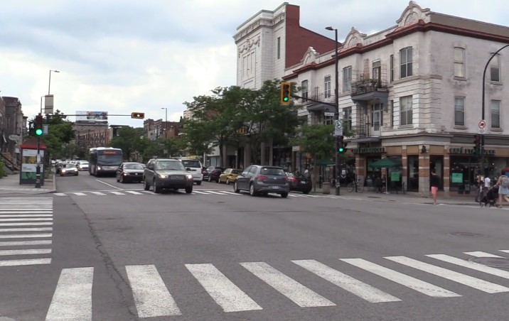 A busy street scene with cars driving and pedestrians crossing at a crosswalk
