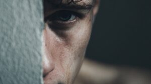 Close-up of a person’s face partially hidden behind a wall, focusing on a serious eye