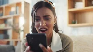 A woman looks shocked and upset as she looks at her smartphone, worried about a possible hacked phone