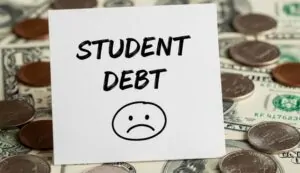 Paper that says "Student debt"with sad emoticon on it, money in the background