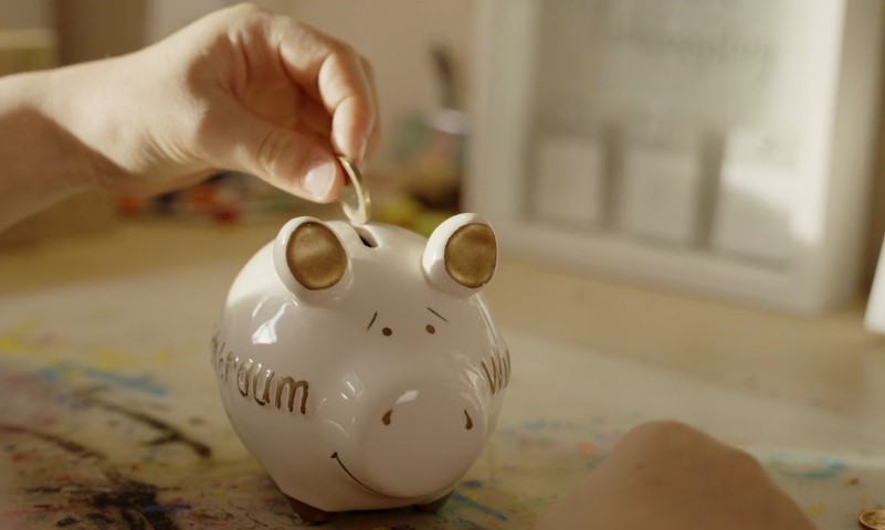 Person inserts a coin into a piggy bank