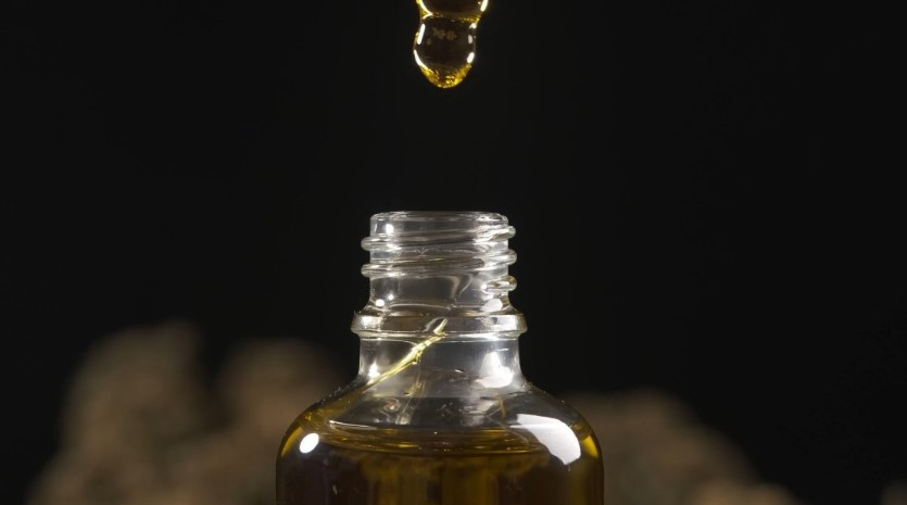 A single drop of oil suspended in mid-air, about to fall into a clear glass bottle
