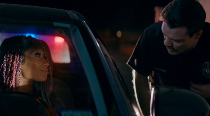 A woman with braided hair is stopped by a police officer at night