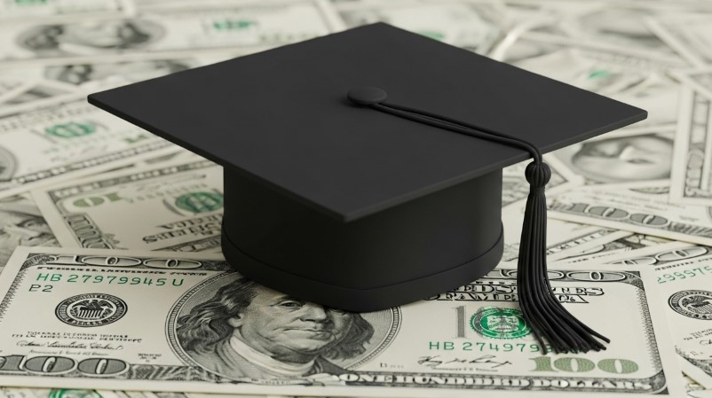 A graduation cap rests atop a bed of US hundred-dollar bills