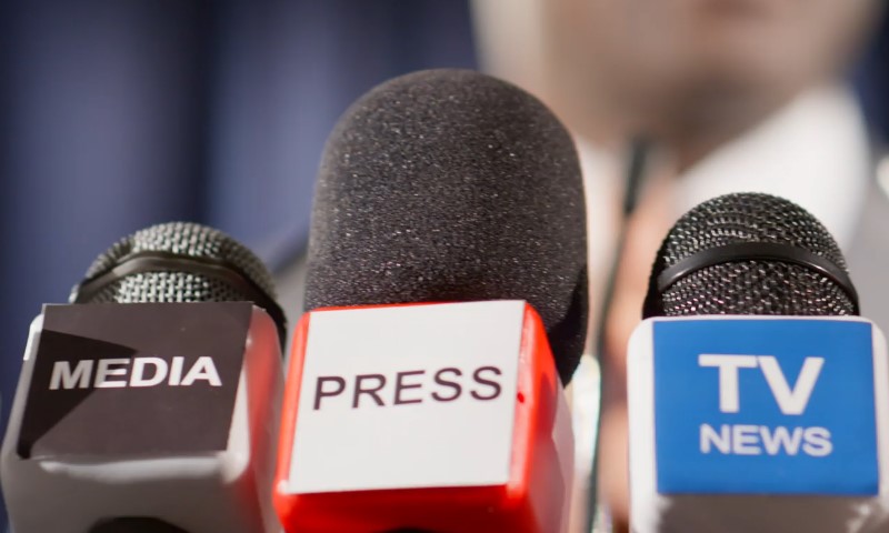 Three microphones labeled 'MEDIA,' 'PRESS,' and 'TV NEWS' positioned closely together during an announcement