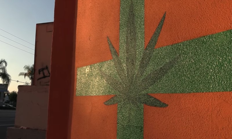 green marijuana leaf painted on a vibrant orange wall