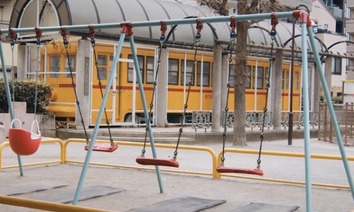 A swing set in front of a bright yellow train, set against a clear blue sky
