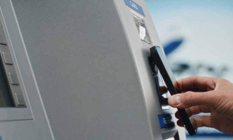 Hand tapping a smartphone against a light gray ATM terminal for contactless transaction
