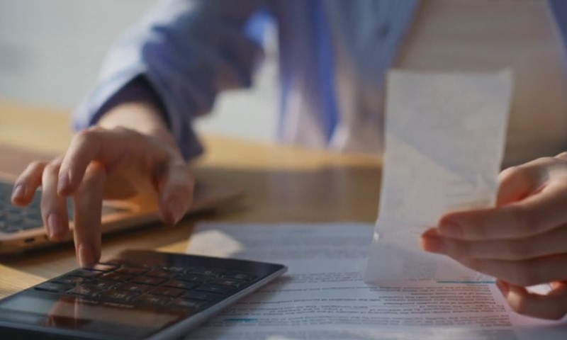 Close-up view of financial record-keeping, showing hands interacting with a mobile device and a paper document