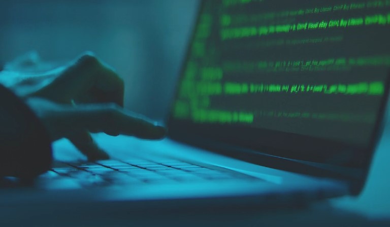 A hacker focused on typing on a laptop computer