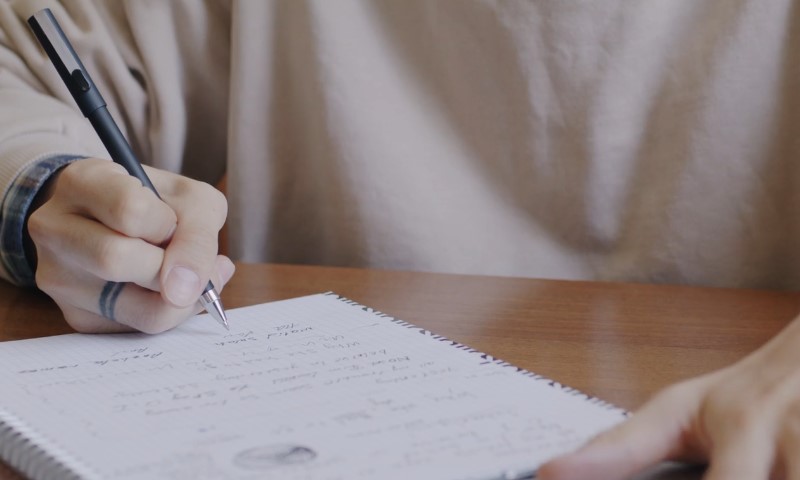 A person writing in a notebook with a pen,