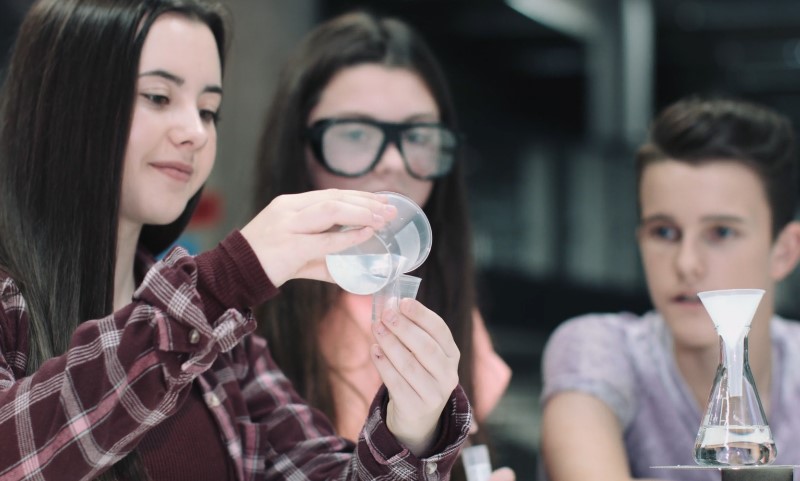 Three focused high school students conduct a clear liquid transfer experiment