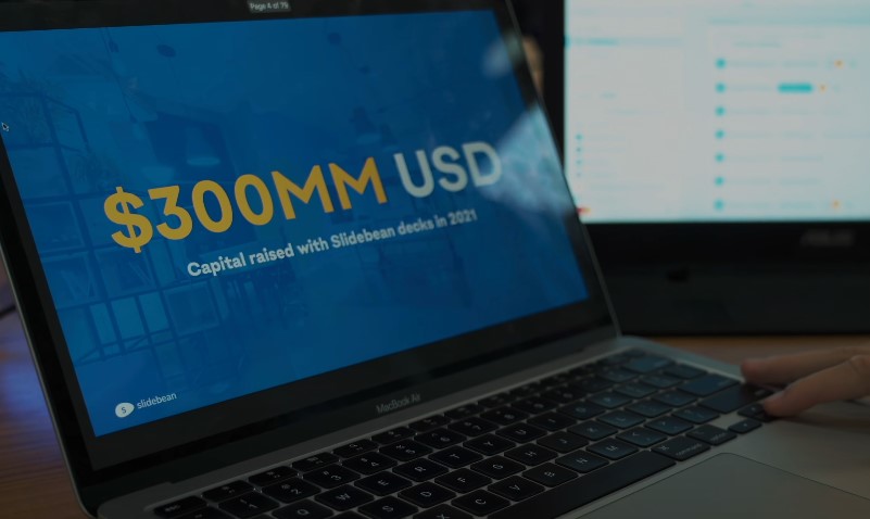 Financial milestone visible on a vibrant blue presentation slide projected onto a MacBook Air screen