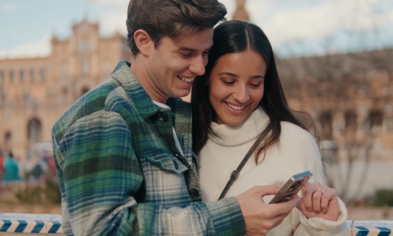 A young couple smiles at their cell phone, sharing a joyful moment together
