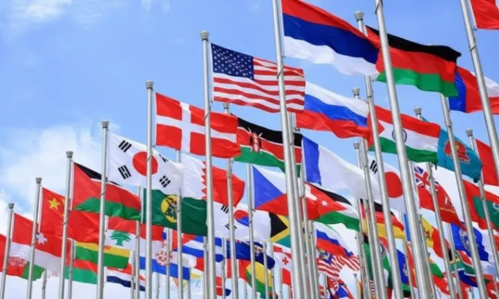 Numerous flags of various colors and designs are waving in the breeze against a clear blue sky
