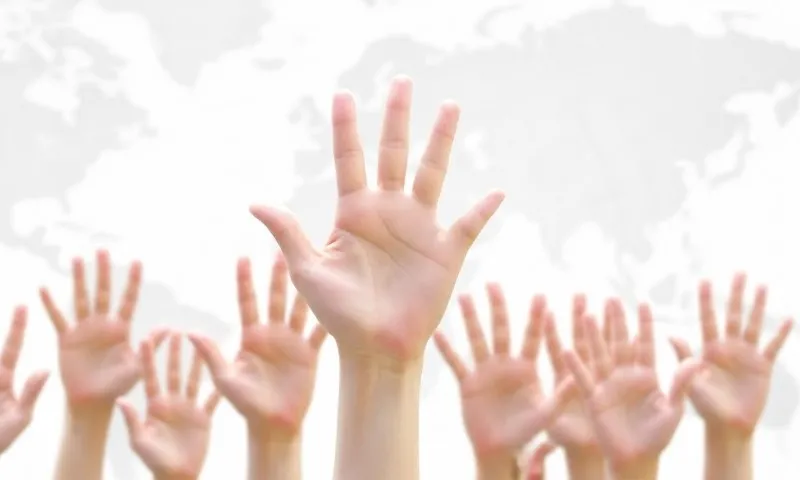 Many hands raised in the air with a world map in the background