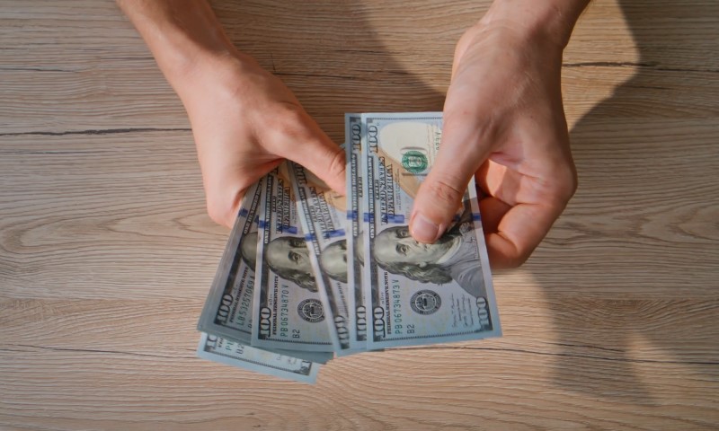 A person holds a stack of cash on a wooden table