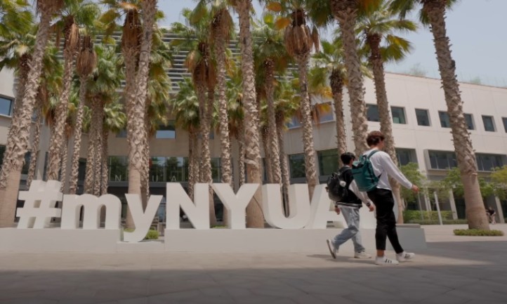 Two people walk past palm trees in front of a building displaying the words "My NYU."