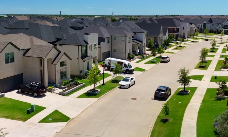A view of a Frisco residential neighborhood with cars parked along the street under clear blue skies