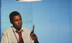 Detective examining a small photo against a backdrop of cool blue window blinds