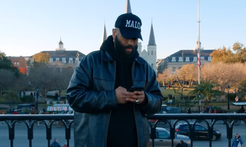 A bearded man wearing a hat is intently looking at his phone