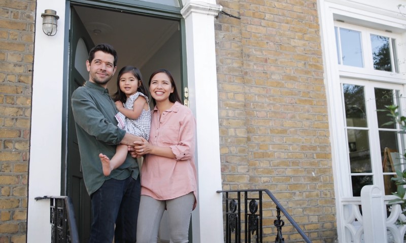 A family of four stands together in front of their house