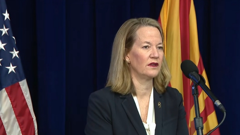 Arizona Attorney General Kris Mayes speaks at a press conference with flags behind her