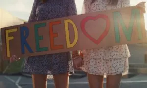 Two women stand together, holding a sign that reads "Freedom," symbolizing their advocacy for liberty and rights