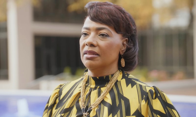 Bernice King in a patterned yellow and black dress and gold necklace stands outdoors