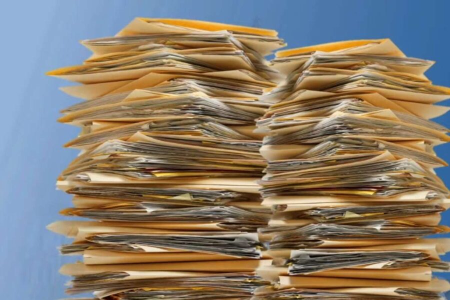 Large stacks of paper files representing end of year documentation and preparation for the next higher education compliance cycle.