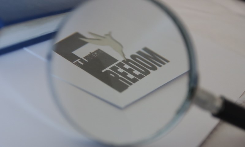 A magnifying glass highlights the word "FREEDOM" on a card. The card also shows a hand formed by negative space, symbolizing liberation and clarity