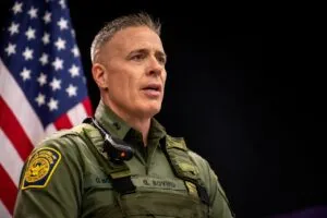 Greg Bovino stands with a U.S. flag in the background