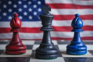 A black king chess piece flanked by red and blue bishops on a chessboard, with the U.S. flag in the background