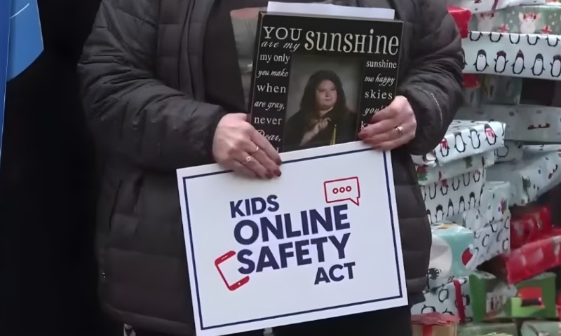 A person holds a poster reading "KIDS ONLINE SAFETY ACT" 