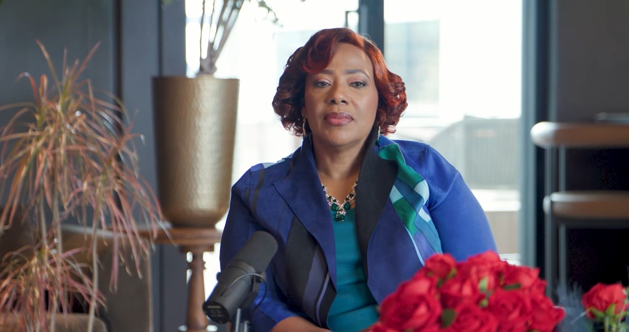 Bernice King in a blue jacket sits at a table with a microphone and red flowers