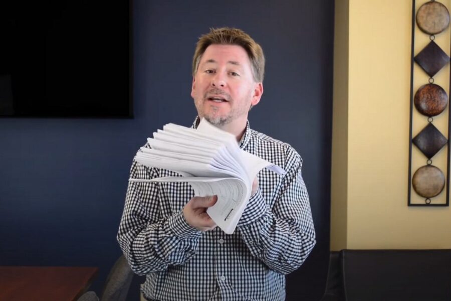 Administrator holding a large stack of documents, symbolizing Form 990 compliance due by May 15 2026 for calendar-year higher education institutions.