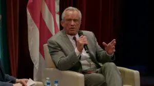 Robert F. Kennedy Jr in a gray suit discusses passionately while holding a microphone