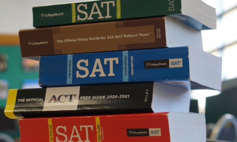 Stack of standardized test prep books, including SAT and ACT guides, on a blurred background