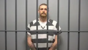 Sean Grayson in black-and-white striped prison uniform stands behind jail bars