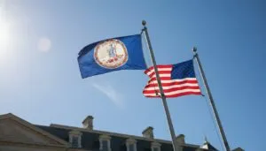 Two flags, Virginia state and U.S., wave on flagpoles against a clear blue sky.