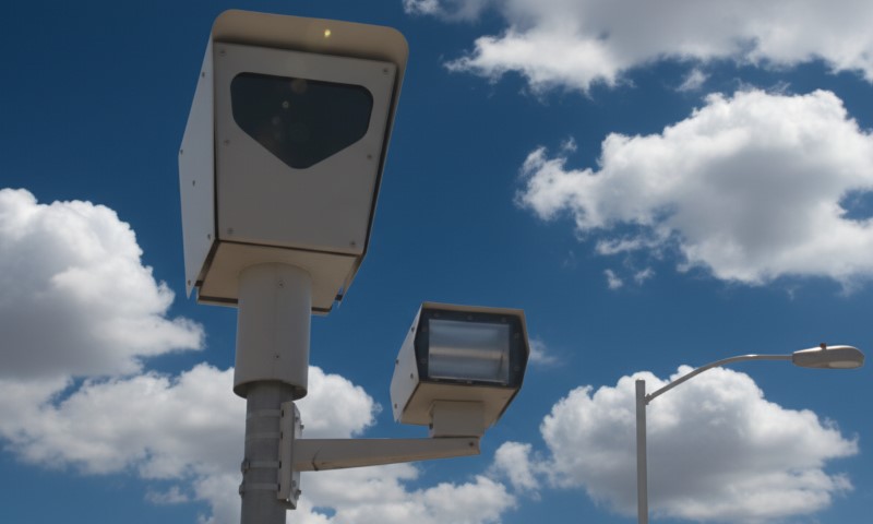 Traffic cameras mounted on a pole against a backdrop of a bright blue sky with scattered clouds