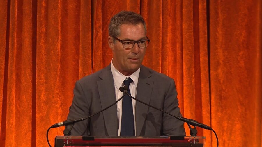 Brad Karp in a gray suit and glasses speaks at a podium